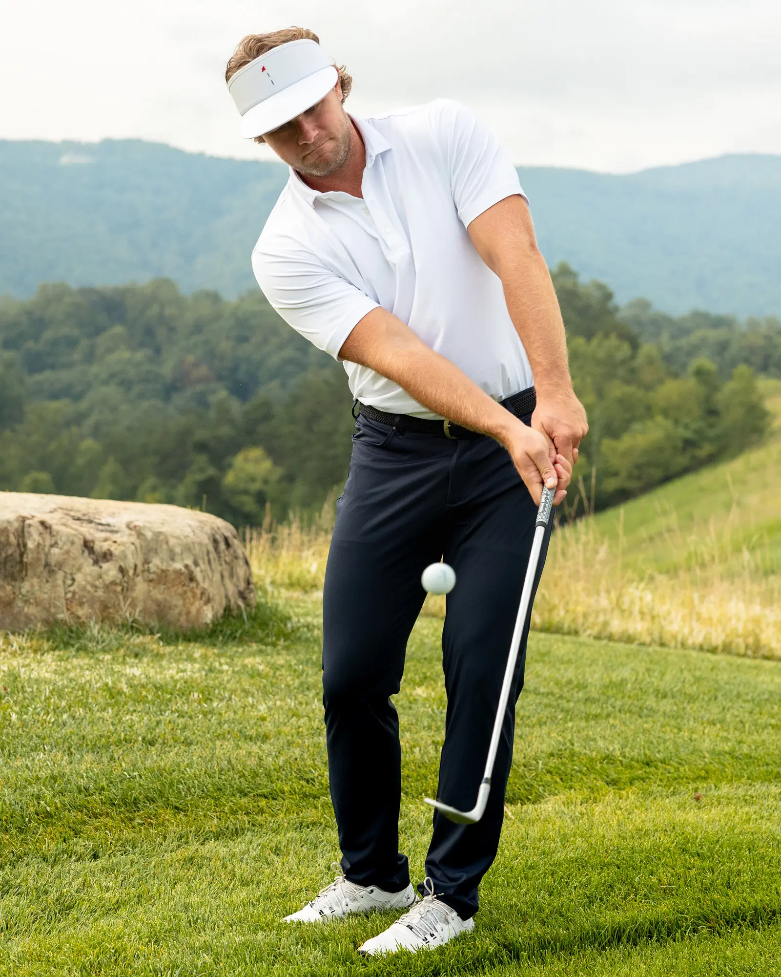 Man dressed in a performance polo, golf visor, and golf pants playing golf in the mountains